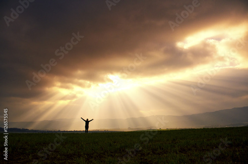 Young happy girl holding her arms up to the sky with dramatically spring sky and beautiful rays. motivation quotes wallpaper concept. photo