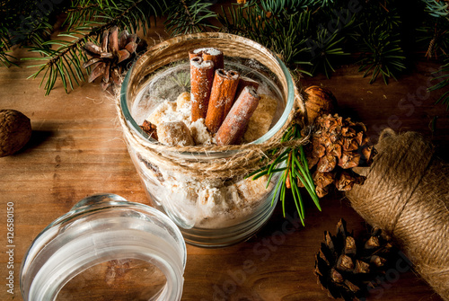Original idea for a Christmas gift: a set of dry ingredients for ginger cookies, decorated in a jar, on a background of branches of the fir, cones, nuts. Copy space, vintage