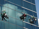 men cleaning glass building by rope access at height