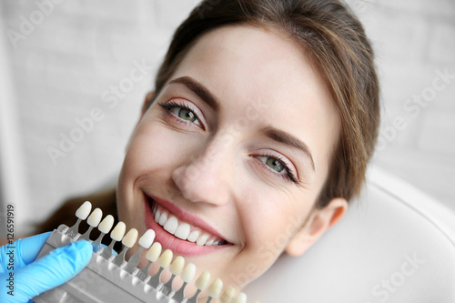 Young woman choosing color of teeth at dentist