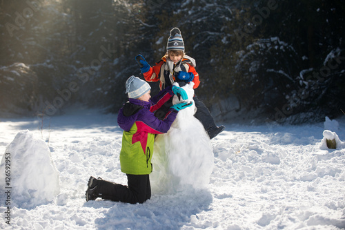 Children playing making snowman, kids play outdoors in winter having fun in christmas time.