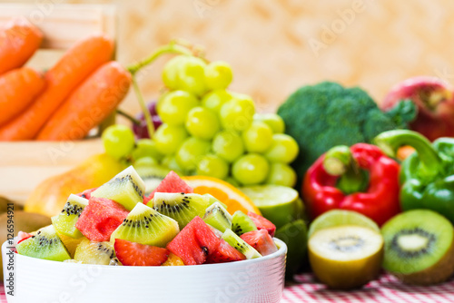 Fruit salad in a white bowl with vegetables background