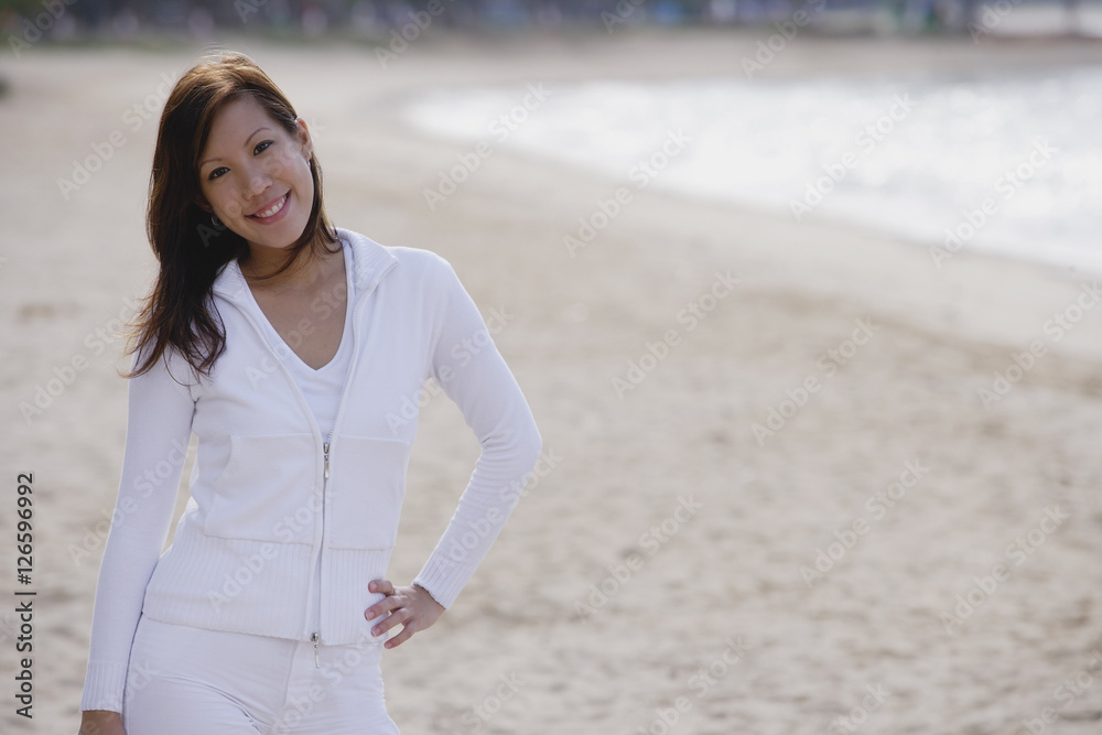 Young woman standing on beach, hand on hip, smiling at camera Young woman standing on beach, hand on hip, smiling at camera