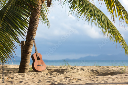 Fototapeta Naklejka Na Ścianę i Meble -  An acoustic guitar standing in the sandy beach under palm tree