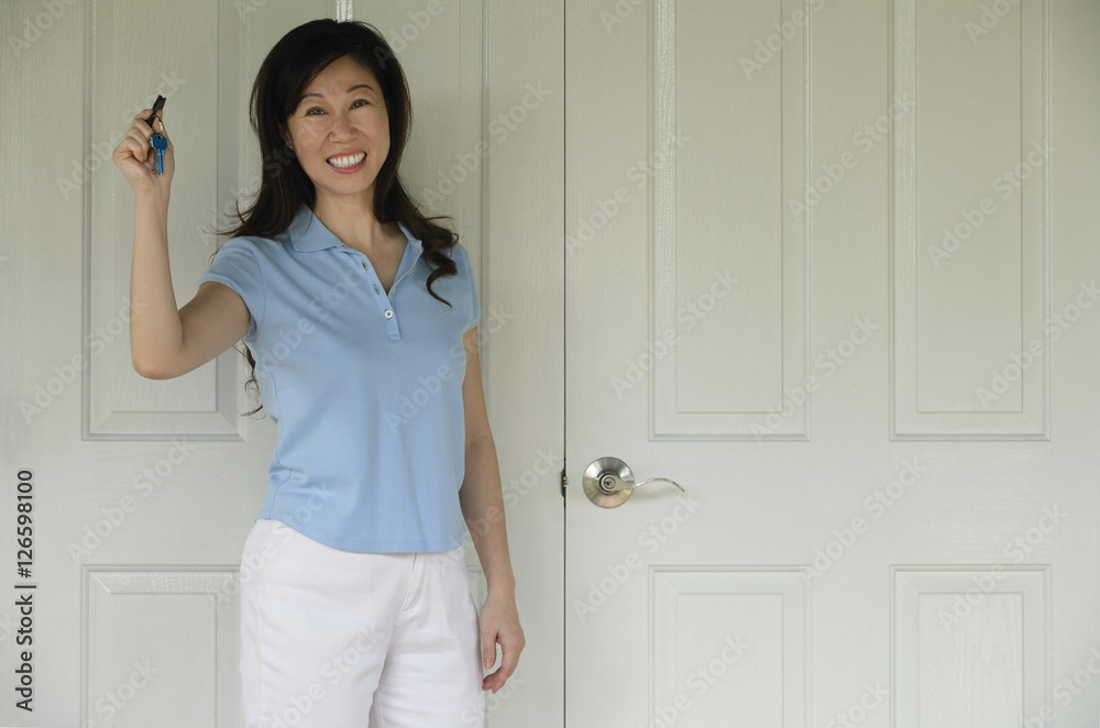 Woman standing next to door, holding house keys, smiling