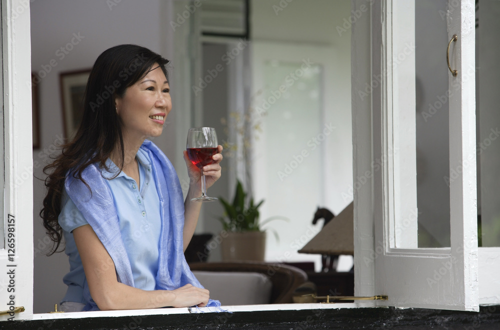 Woman at home, looking out of the window, holding wine glass