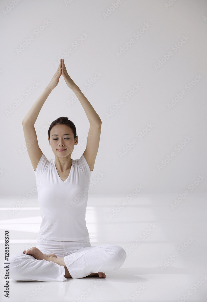 Woman sitting cross legged on floor in yoga posture, with arms raised over  head in prayer Stock Photo | Adobe Stock