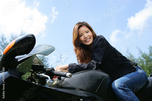 Young woman sitting on motorcycle, smiling at camera, low angle view © Alexander