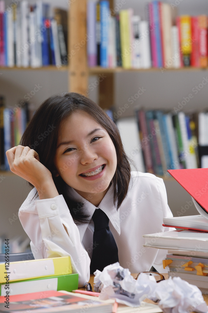 Young woman in library, surrounded by books and crumpled paper