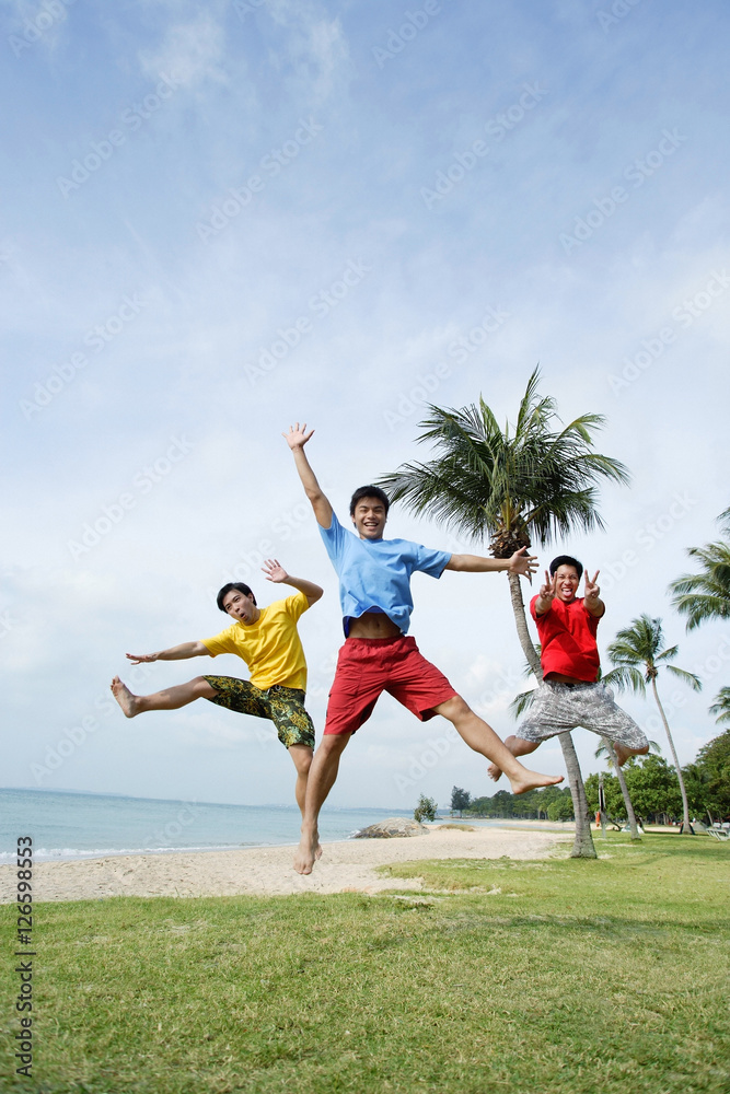 Three men on beach, jumping in air, looking at camera Three men on beach, jumping in air, looking at camera