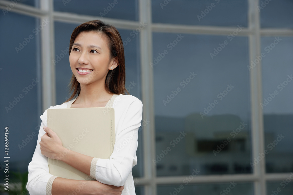 Female executive hugging folders, smiling, looking away Female executive hugging folders, smiling, looking away