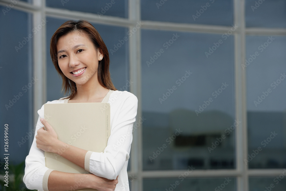Female executive hugging folders, smiling at camera, portrait