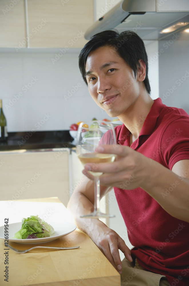 Man sitting down for a meal, raising wine glass toward camera