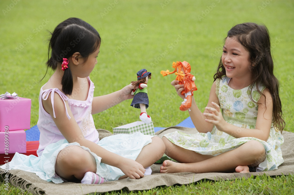 Two girls sitting on picnic blanket, playing with dolls