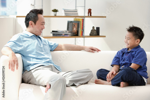 Father and son sitting on sofa, smiling at each other