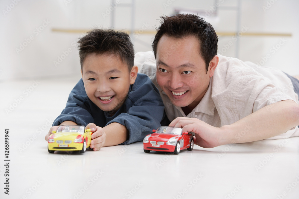 Father and son lying on floor, playing with toy cars