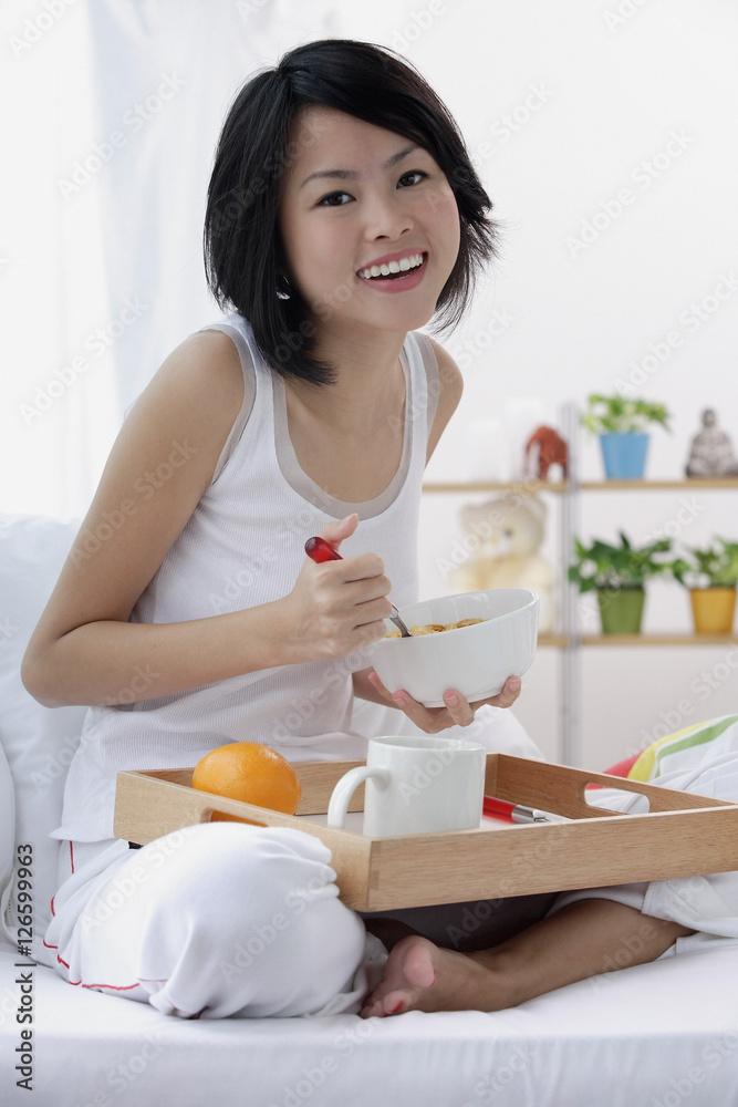 Young woman having breakfast in bed, smiling at camera Young woman having breakfast in bed, smiling at camera
