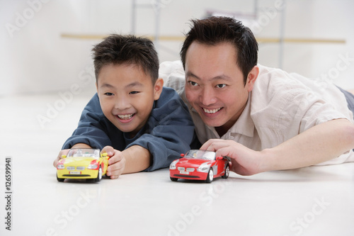 Obraz na płótnie Father and son lying on floor, playing with toy cars w salonie