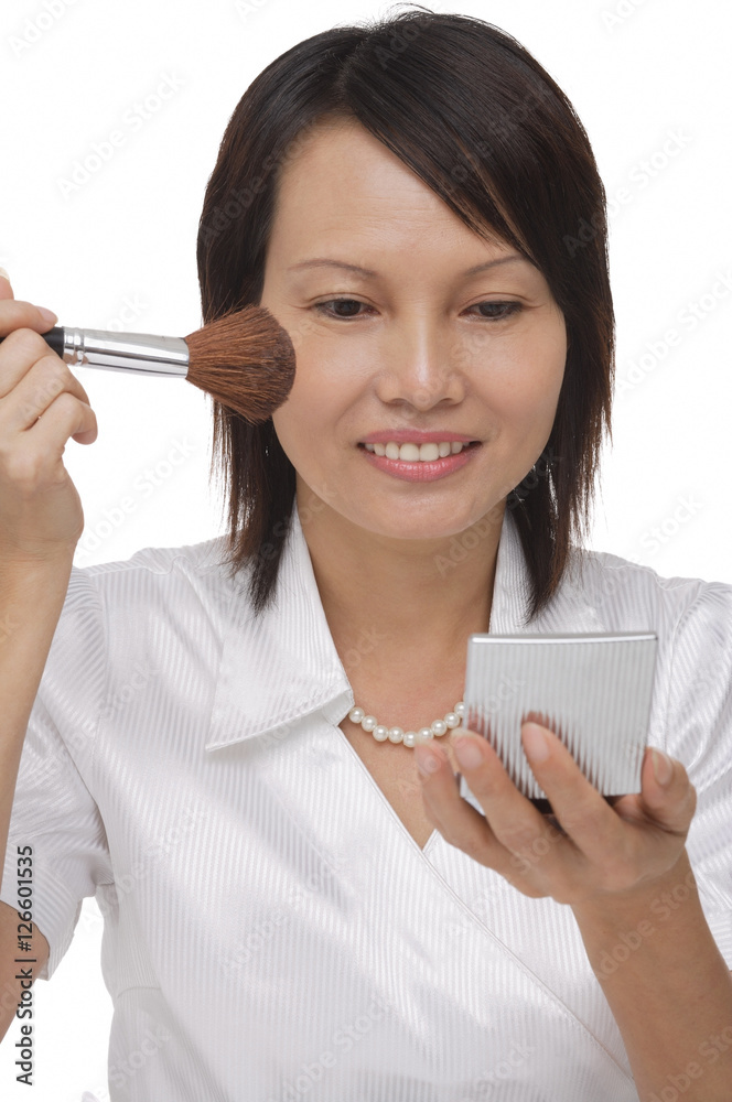 Woman applying cosmetics while looking into compact mirror Woman applying cosmetics while looking into compact mirror