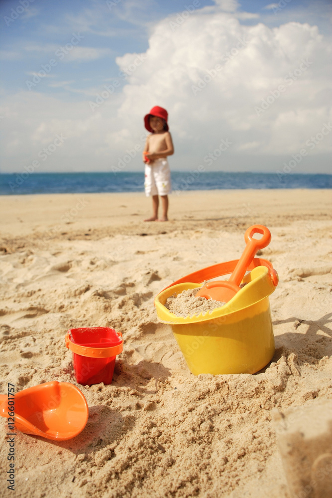 Young boy on beach, beach bucket and toys in foreground Young boy on beach, beach bucket and toys in foreground