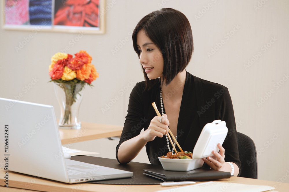 A woman eats lunch at her desk while she works