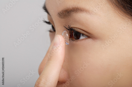 A young woman puts a contact lens in