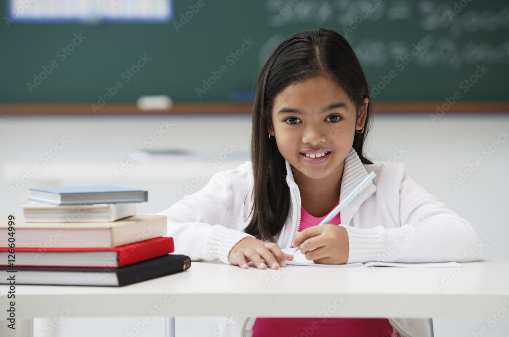 Girl with pen sitting at school desk smiling at camera Girl with pen sitting at school desk smiling at camera