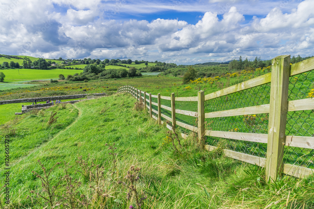 Rural landscape scene with a long fence and green fields, taken in Ireland.