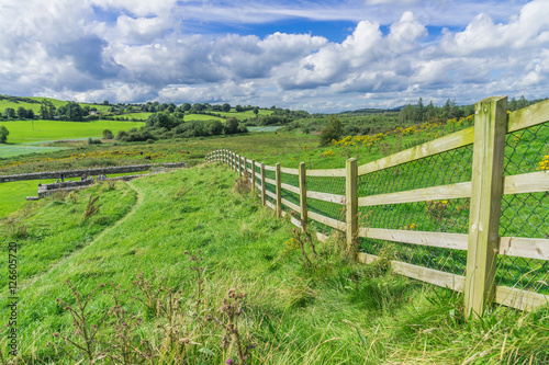 Rural landscape scene with a long fence and green fields, taken in Ireland.