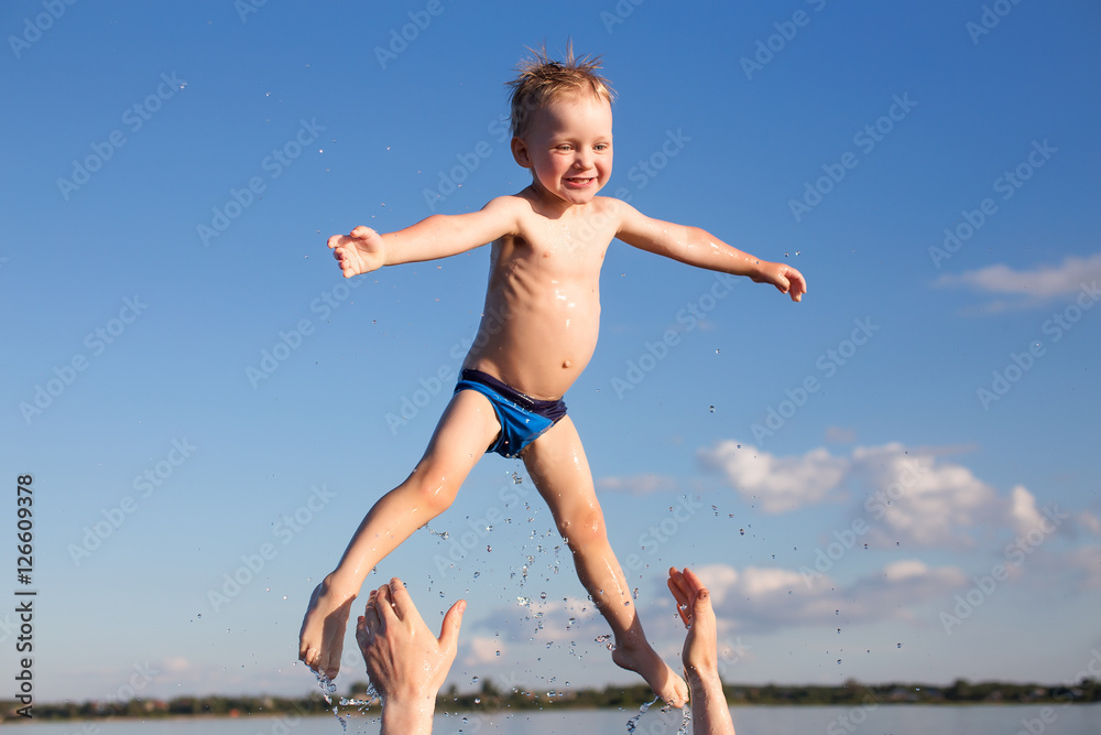 Obraz premium male hands tossing up the kid in the water. fun in the water. father throws the little boy up high. the concept of family lifestyle, summer vacation.