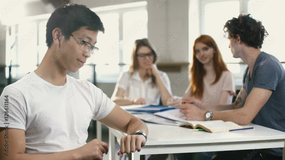 Concentrated businessman using smart watch at the table in office with his team on background Concentrated businessman using smart watch at the table in office with his team on background
