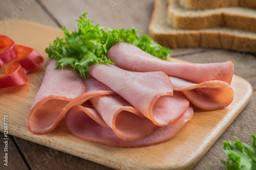 Sliced ham on wooden plate and bread slices