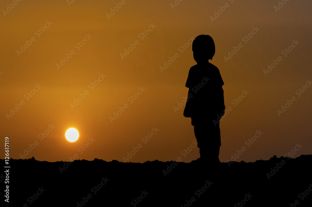 The silhouette of young boy standing with looking sunset