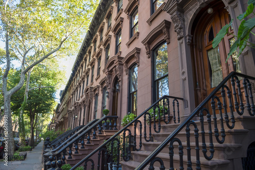 Leafy summer view of the row of stoops on one of the iconic streets of the neighborhood of Brownstone Brooklyn in New York City