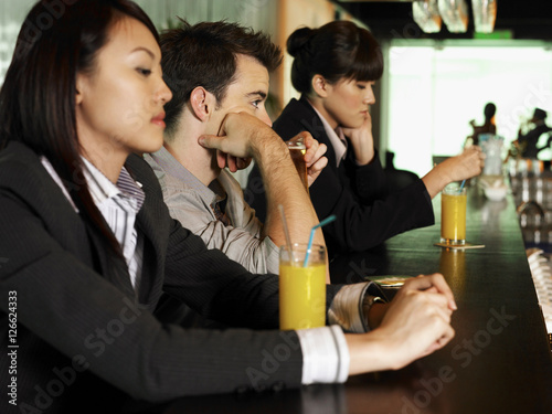 three people sitting at bar with drinks