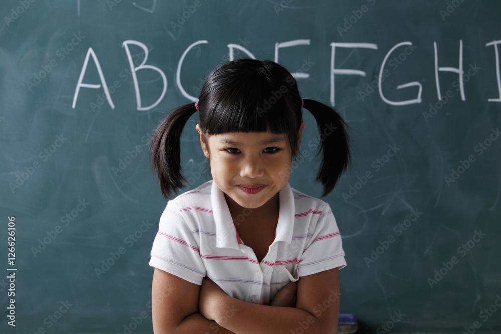 young girl with pony tails smiling in front of chalk board