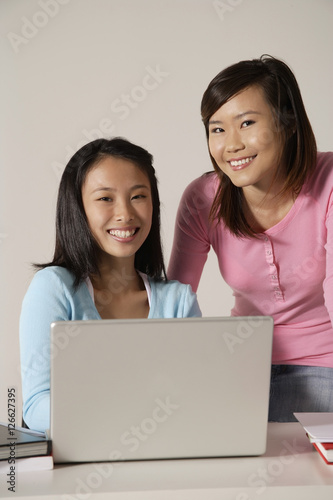Two women at laptop, smiling.