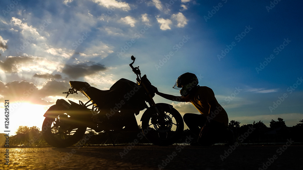 Fototapeta premium Silhouette biker with his motorbike beside the natural lake and beautiful twilight sky.