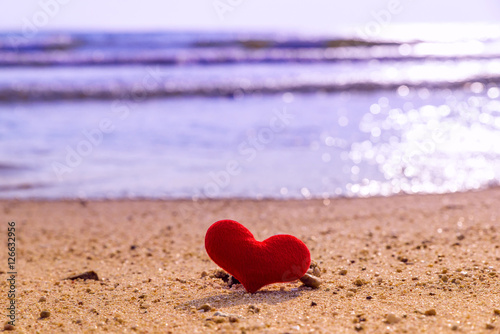 Red textile heart in the sand on the background of beach and sea. Toned