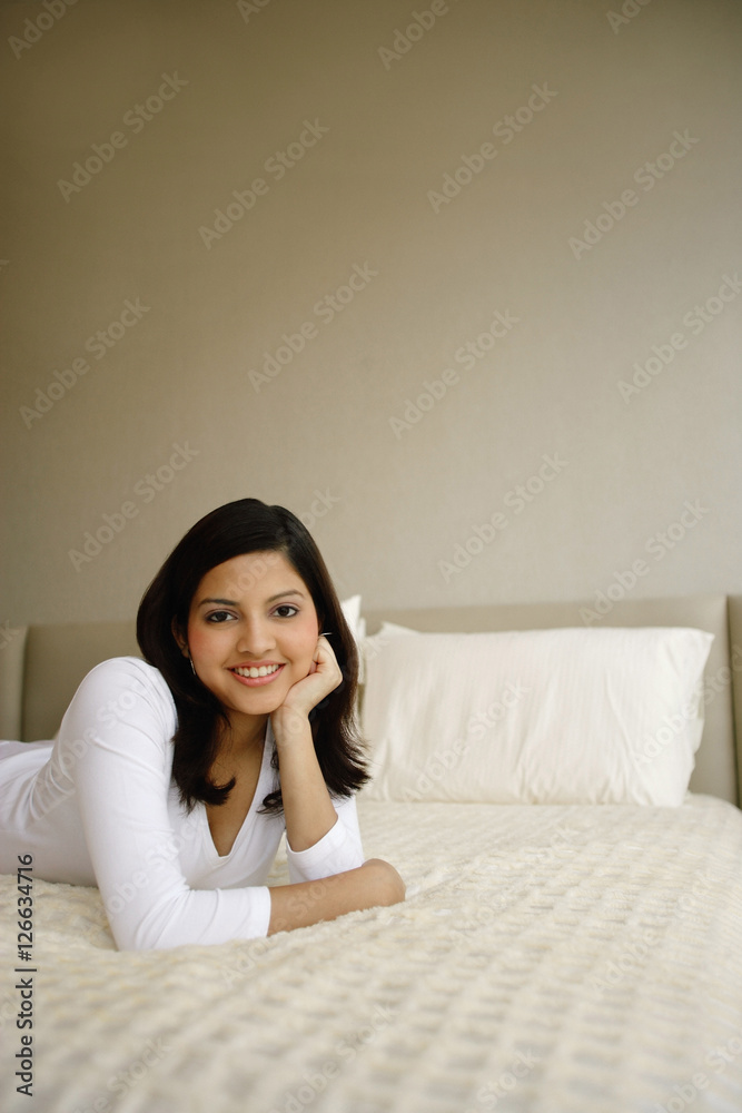 Woman lying on bed, hand in chin, smiling at camera Woman lying on bed, hand in chin, smiling at camera
