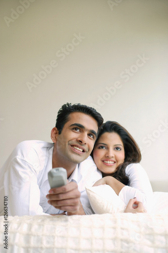 Couple lying on bed, side by side, watching TV