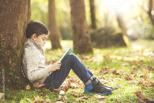 Little boy reading a book in the park. Learning and education concept