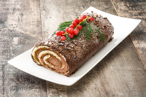 Фотография Chocolate yule log christmas cake with red currant on wooden background