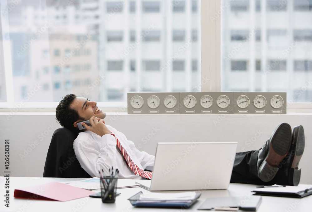 Businessman in office, using mobile phone, feet up on desk Businessman in office, using mobile phone, feet up on desk