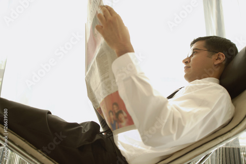 Businessman reclining on chair, reading newspaper