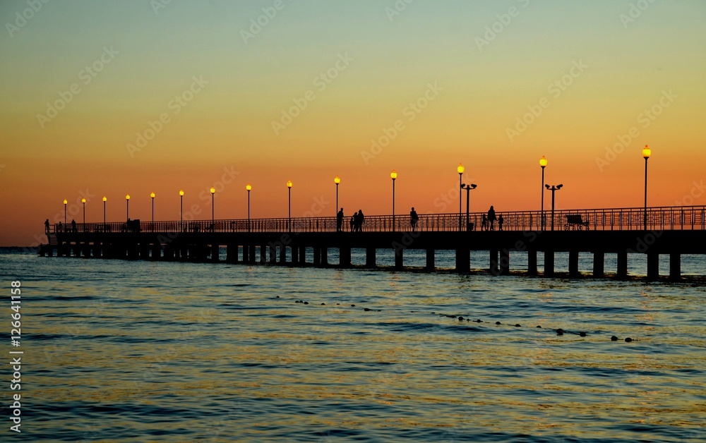 Completion holiday season on Black Sea coast of Russia. Few vacationers walking on sea pier after sunset