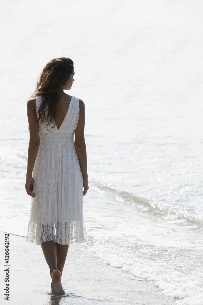 back view of woman wearing a white dress and walking a long the beach back view of woman wearing a white dress and walking a long the beach