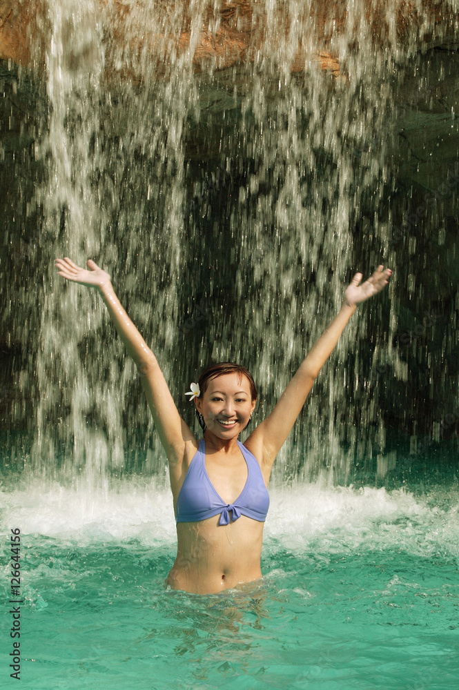 Young woman in swimming pool, water cascading on her