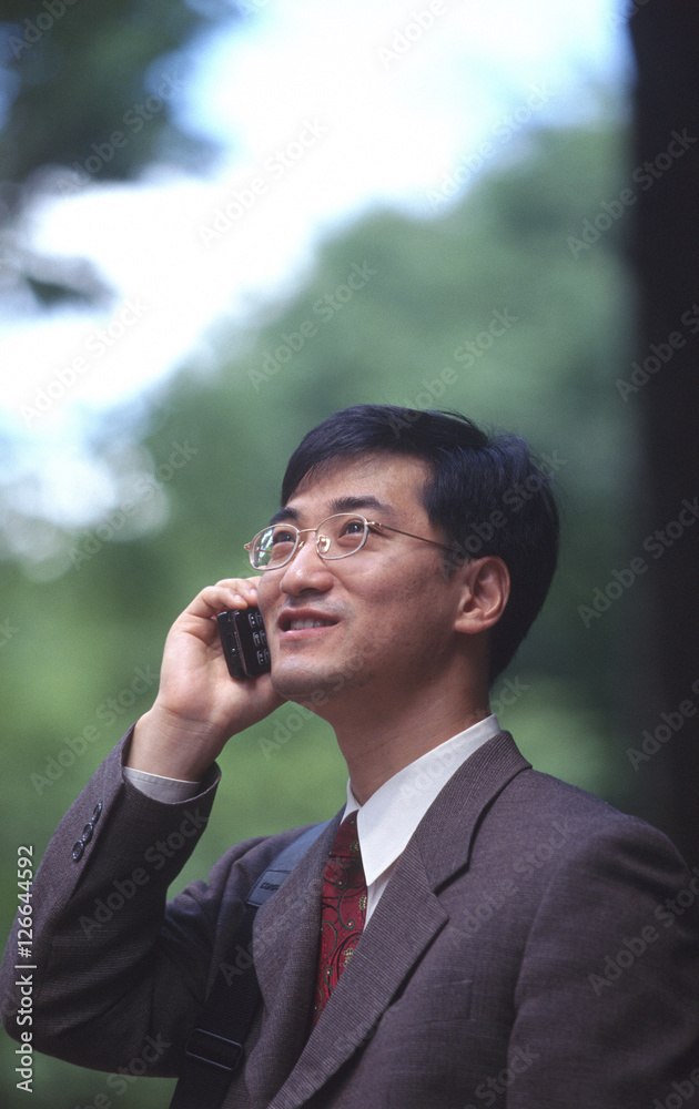 Male executive talking on cellular phone, trees behind Male executive talking on cellular phone, trees behind