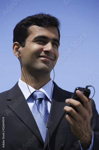 Indian businessman listening to music outside.